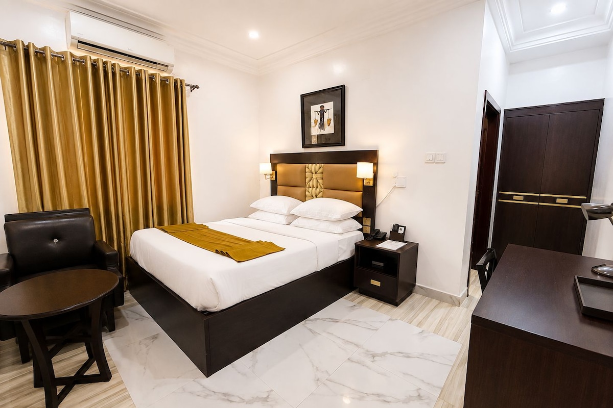 Een hotelkamer met een bed, nachtkastje, stoel, bureau en kledingkast.