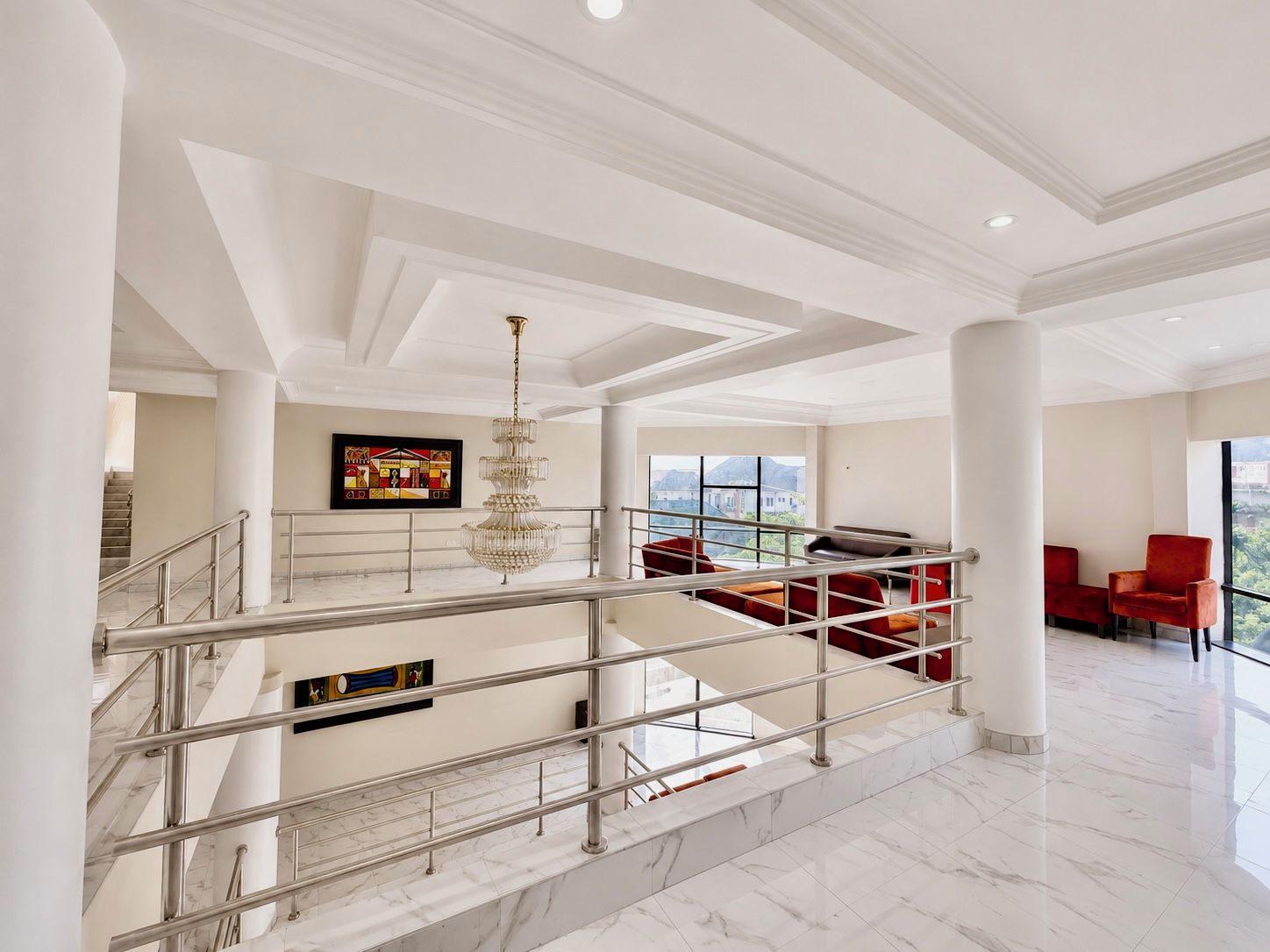 Un interior espacioso con una escalera de mármol, un candelabro y asientos rojos.