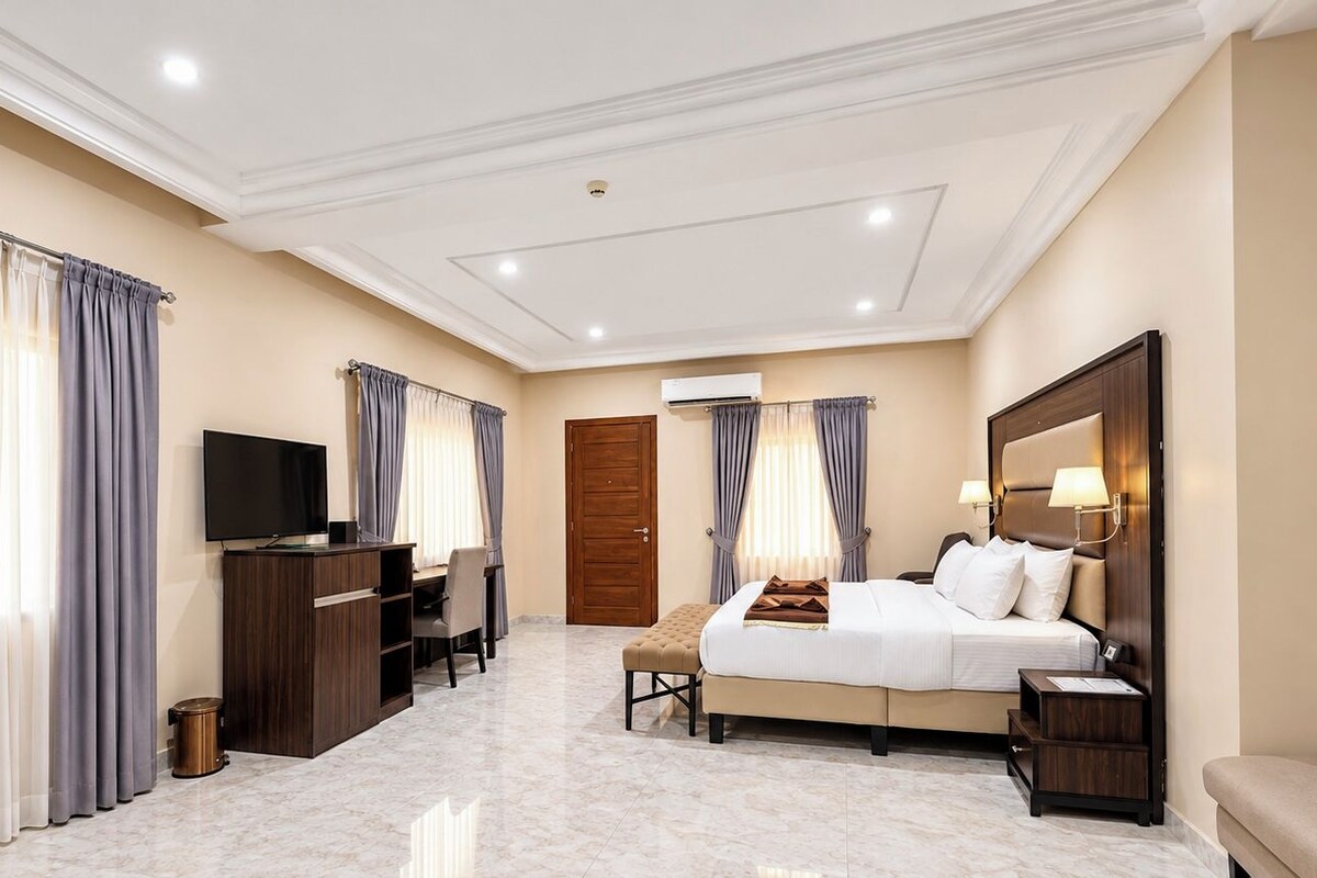 Una habitación de hotel con cama, mesita de noche, televisor, escritorio y silla.