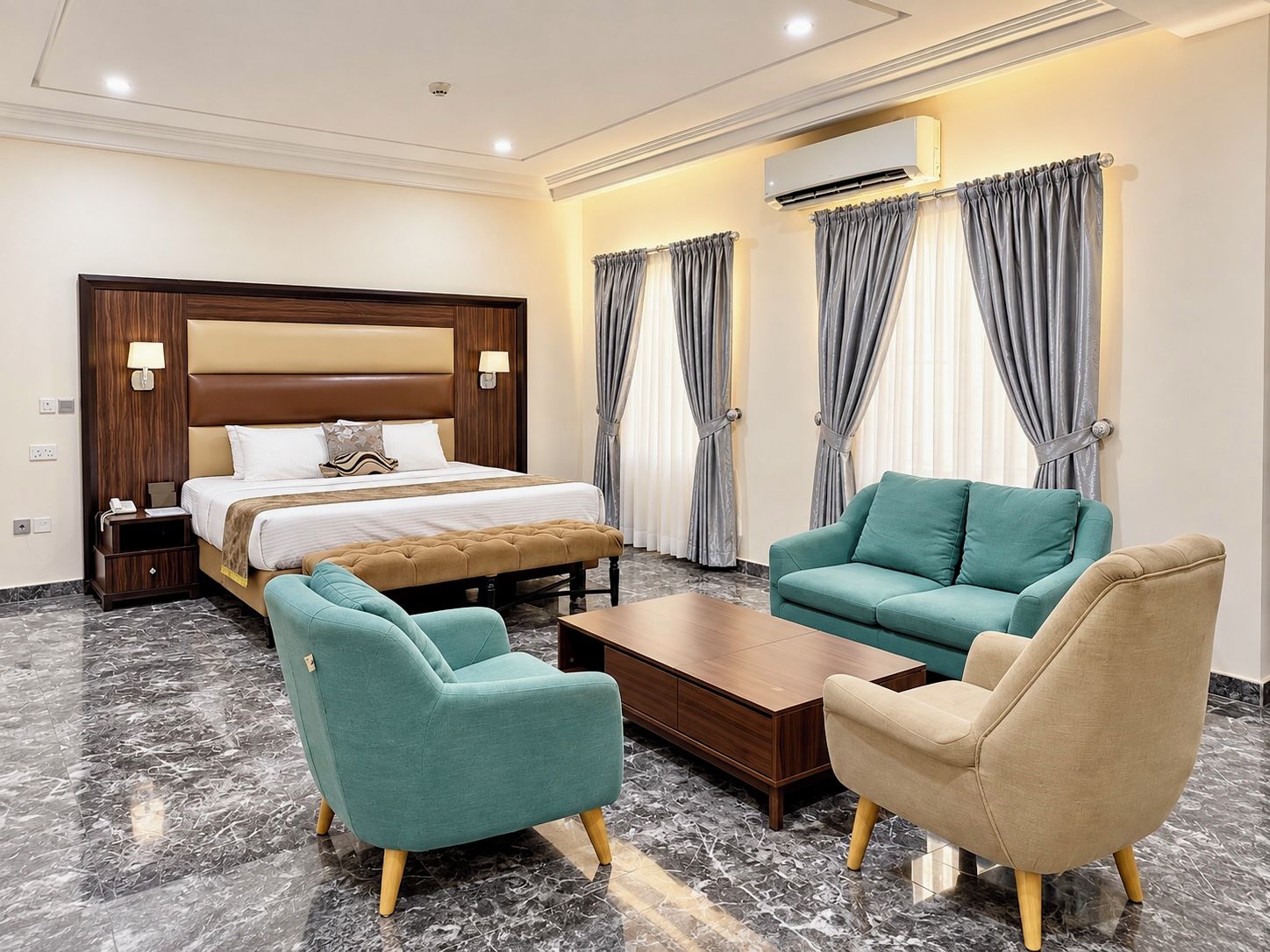Una habitación de hotel con una cama, dos sillones, una mesita de centro y una mesita de noche.
