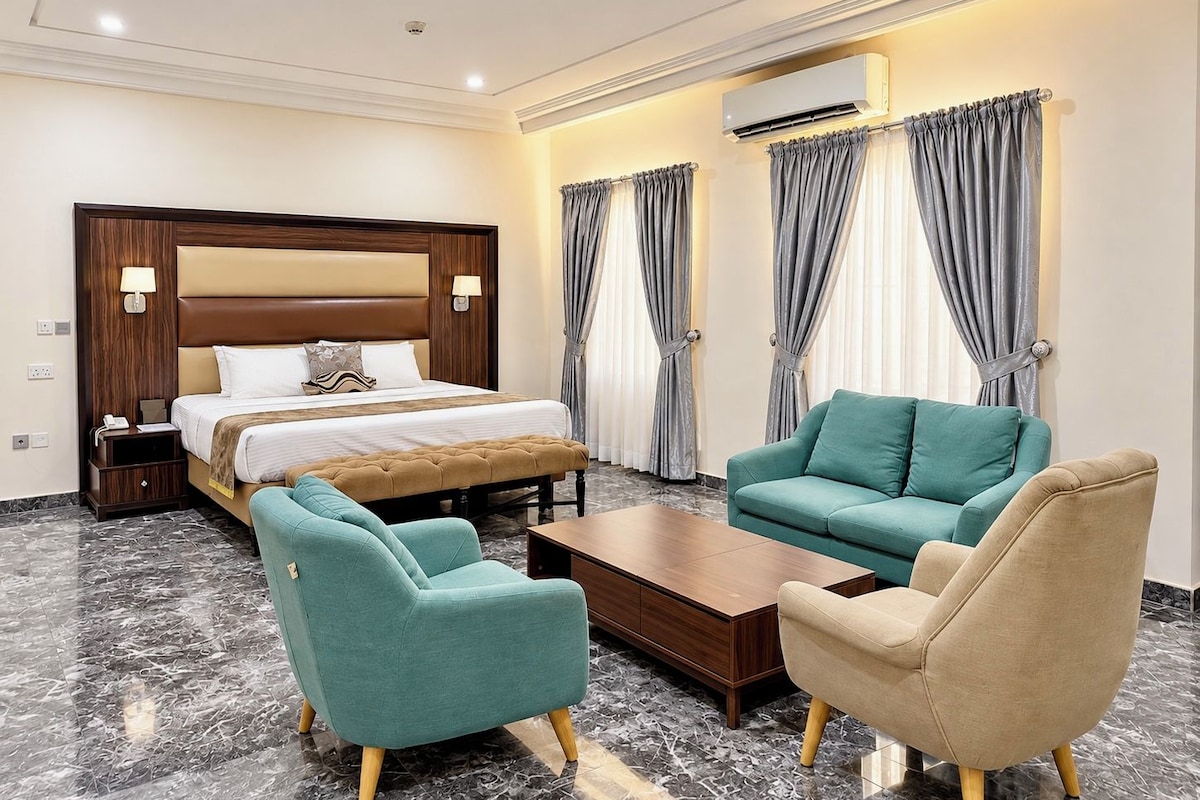Een hotelkamer met een bed, twee fauteuils, een salontafel en een nachtkastje.