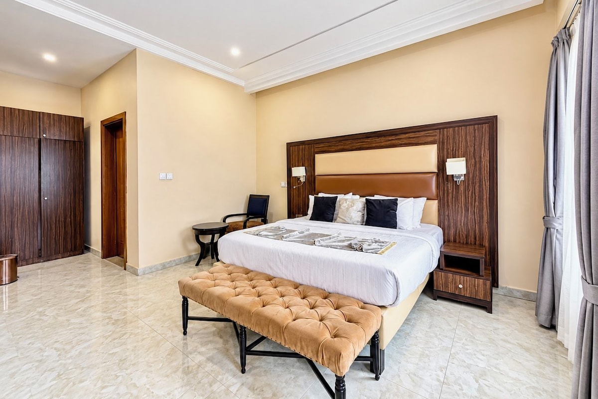 Een hotelkamer met een groot bed, een bankje, een bureau en een kledingkast.