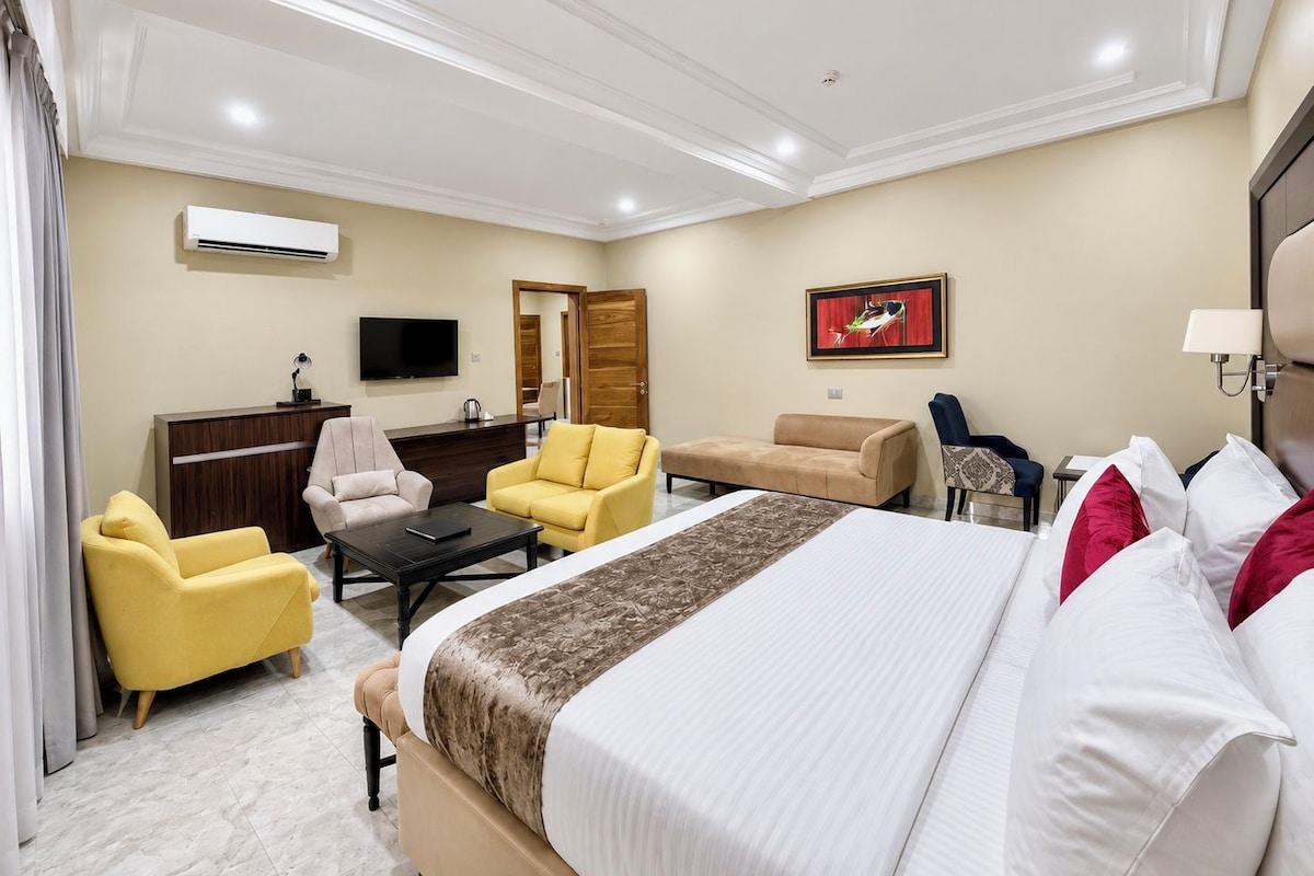 Een hotelkamer met een bed, twee fauteuils, een bank, een bureau, een televisie en een airconditioner.
