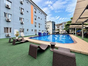 Una piscina con sillas y mesas de descanso, rodeada por un edificio con varias ventanas y unidades de aire acondicionado.