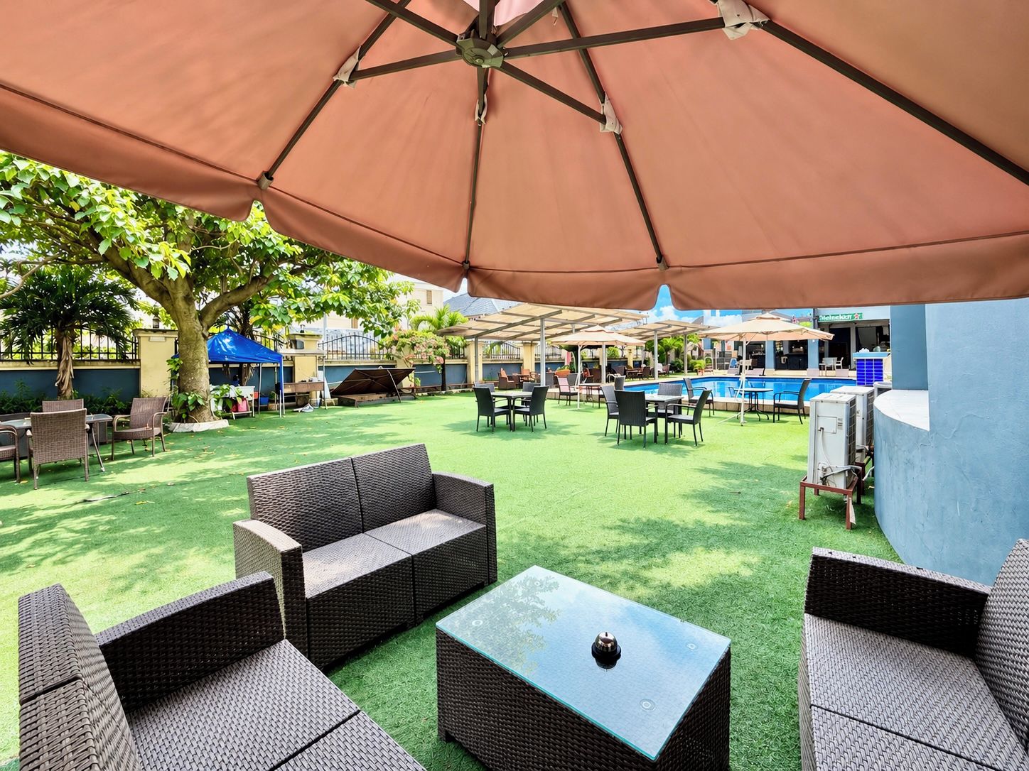 Un espace extérieur aménagé en terrasse, avec des meubles en osier, une piscine et des parasols.