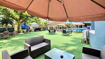 Un espace extérieur aménagé en terrasse, avec des meubles en osier, une piscine et des parasols.