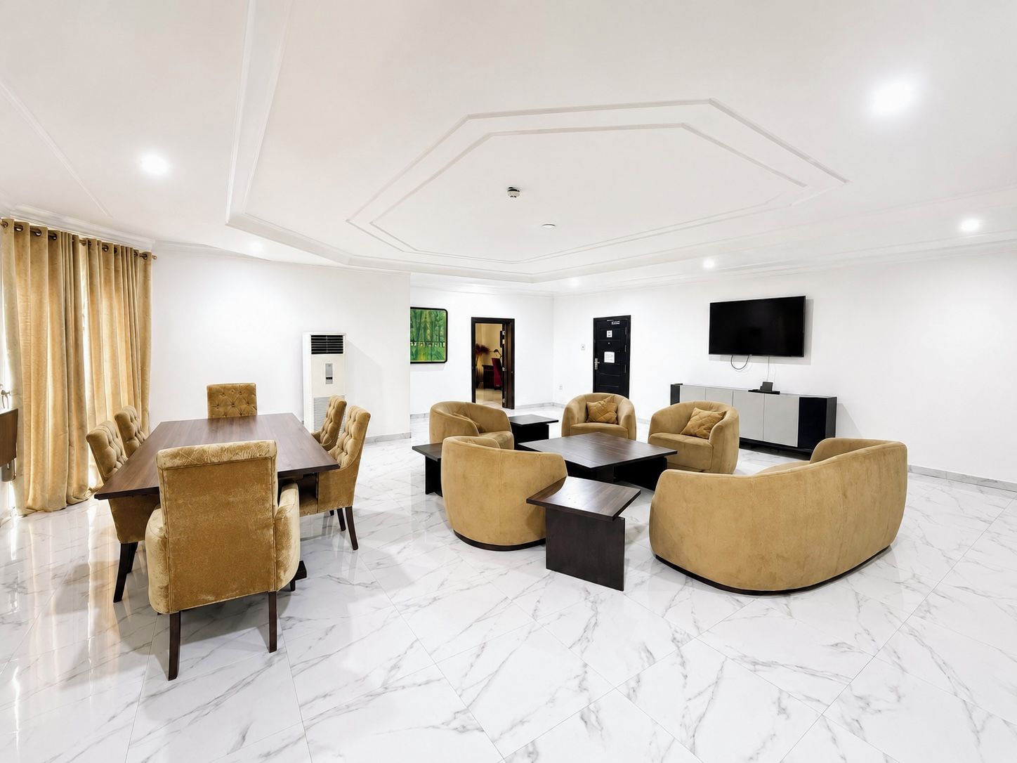 A hotel room with a dining area, seating, a flat-screen TV, and a door.