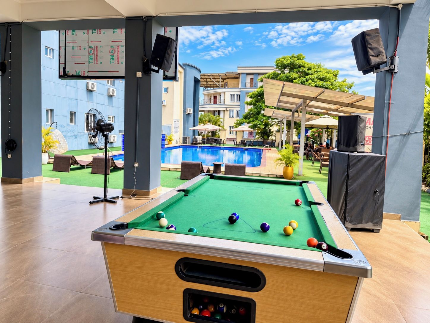 A pool table with balls, a pool table, and a view of a pool and outdoor seating area.