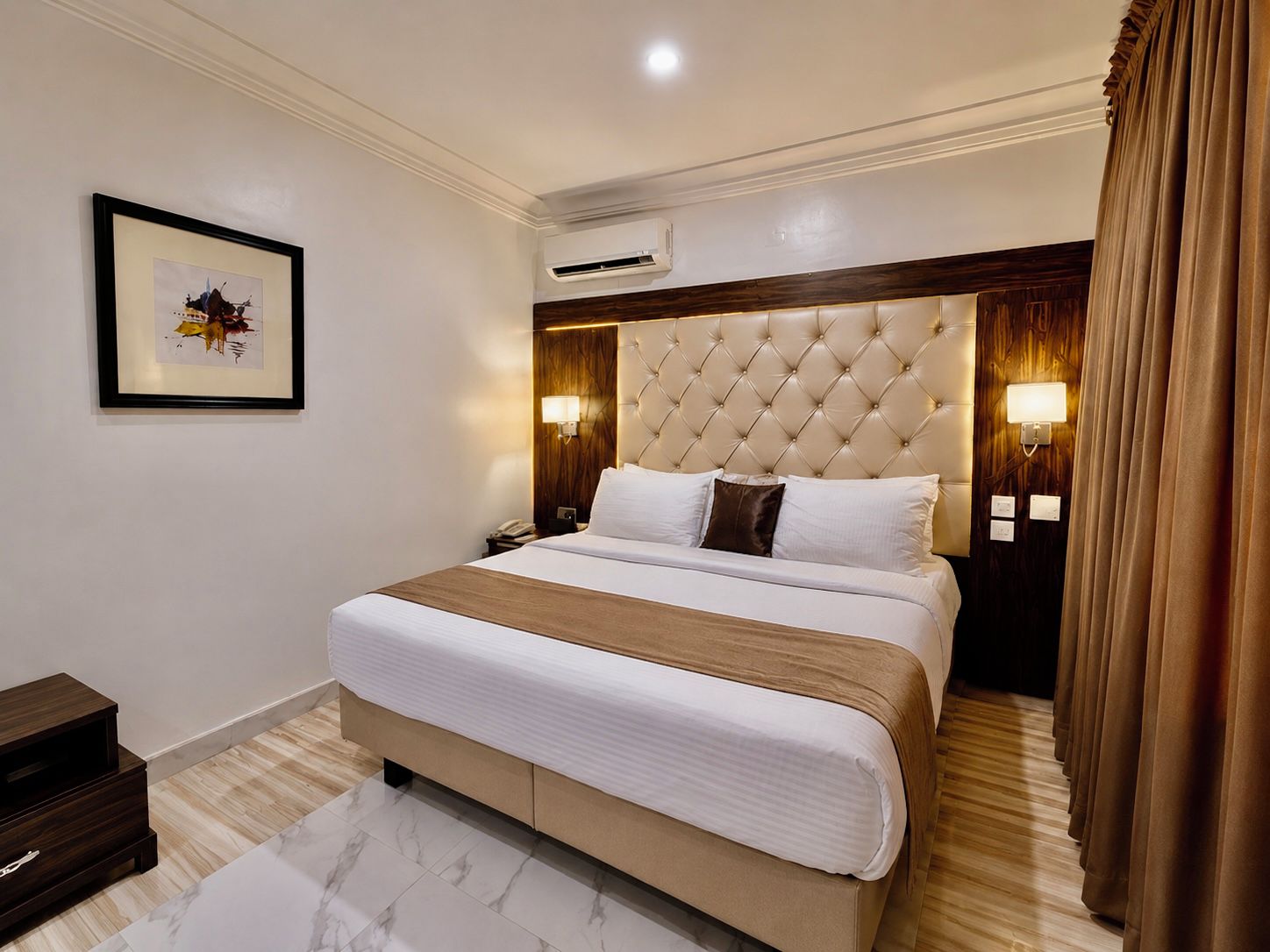 A hotel room with a large bed, two bedside lamps, a framed picture on the wall, and a wooden nightstand.