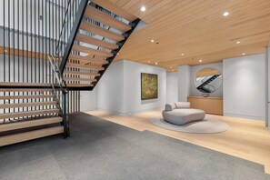 A modern interior with a wooden staircase, a round seating area, and a large mirror. - Just Listed: New Ski Residence, Views, Gym, Hot tub (Whistler)