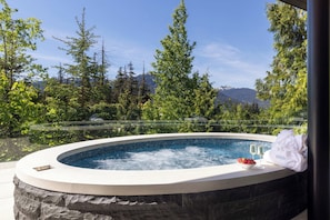 A hot tub with a mountain view, surrounded by trees and a stone wall. - Just Listed: New Ski Residence, Views, Gym, Hot tub (Whistler)