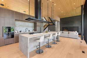 A modern kitchen with a central island, bar stools, a built-in oven, and a staircase leading to an upper level. - Just Listed: New Ski Residence, Views, Gym, Hot tub (Whistler)