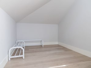 Ein Zimmer mit schrägem Dach, weißen Wänden und Holzboden.