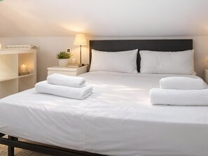 A neatly made bed with white linens and two folded towels, a bedside lamp, a small potted plant, and a nightstand with a book and a candle. - Cozy Accommodation, Central Madrid (Madrid)