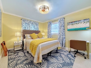 A hotel room with a bed, a desk, a chair, a lamp, a painting, and a patterned rug. - Luxury Florida Retreat with Pool & Exceptional Outdoor Living (St. Petersburg)