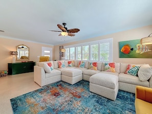A living room with a sectional sofa, a ceiling fan, a colorful rug, and a large window with shutters. - Luxury Florida Retreat with Pool & Exceptional Outdoor Living (St. Petersburg)