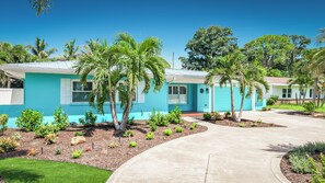 A modern two-story house with a blue exterior, a driveway, and a well-maintained garden with palm trees and shrubs. - Luxury Florida Retreat with Pool & Exceptional Outdoor Living (St. Petersburg)