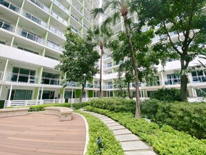 A multi-story hotel with a central courtyard featuring a curved walkway, palm trees, and a variety of shrubs. - Citispace Suites Azure Urban Resort  (Parañaque)
