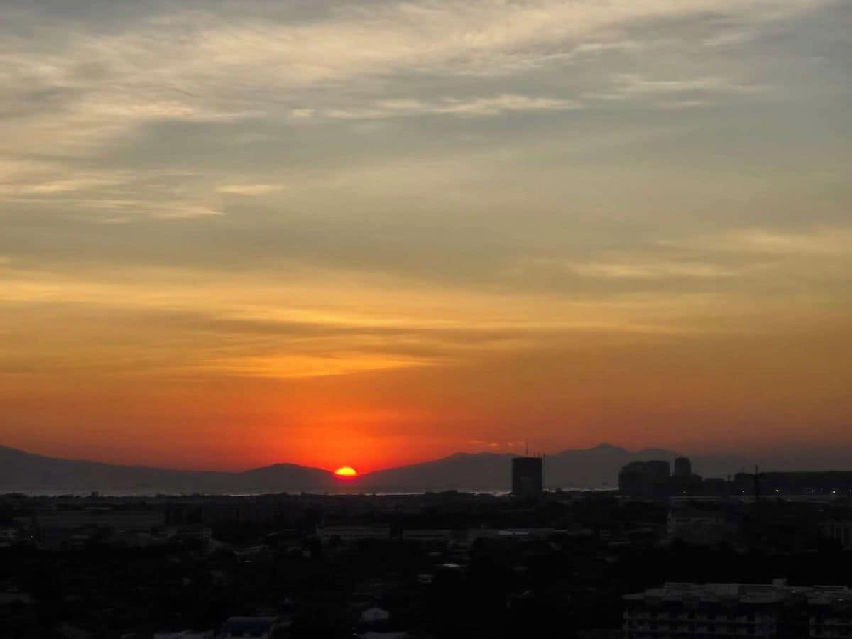 A sunset over a cityscape with buildings and a mountain in the background.