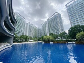 A modern hotel with a swimming pool surrounded by high-rise buildings and greenery. - Citispace Suites Azure Urban Resort  (Parañaque)