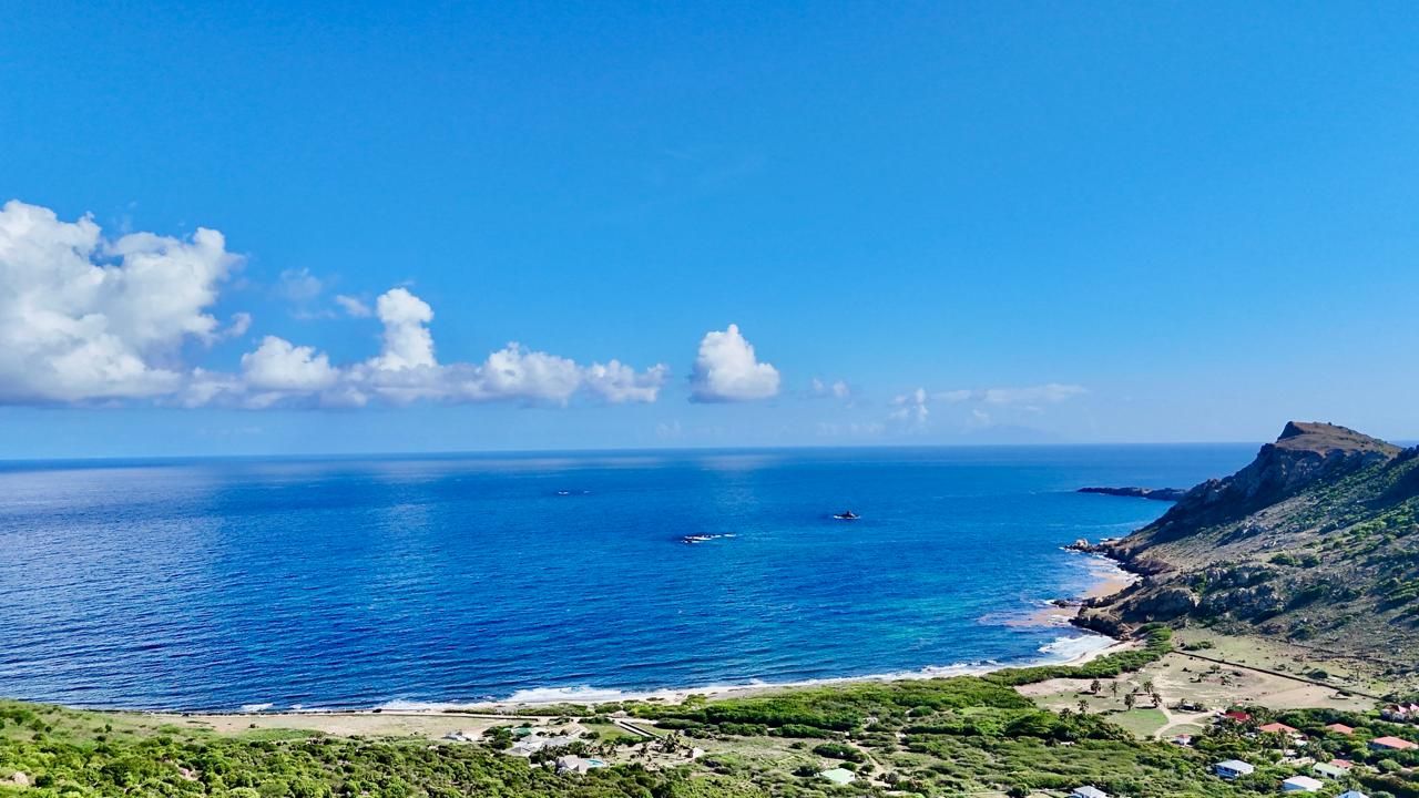 A coastal landscape with a clear sky, a beach, and a mountain.