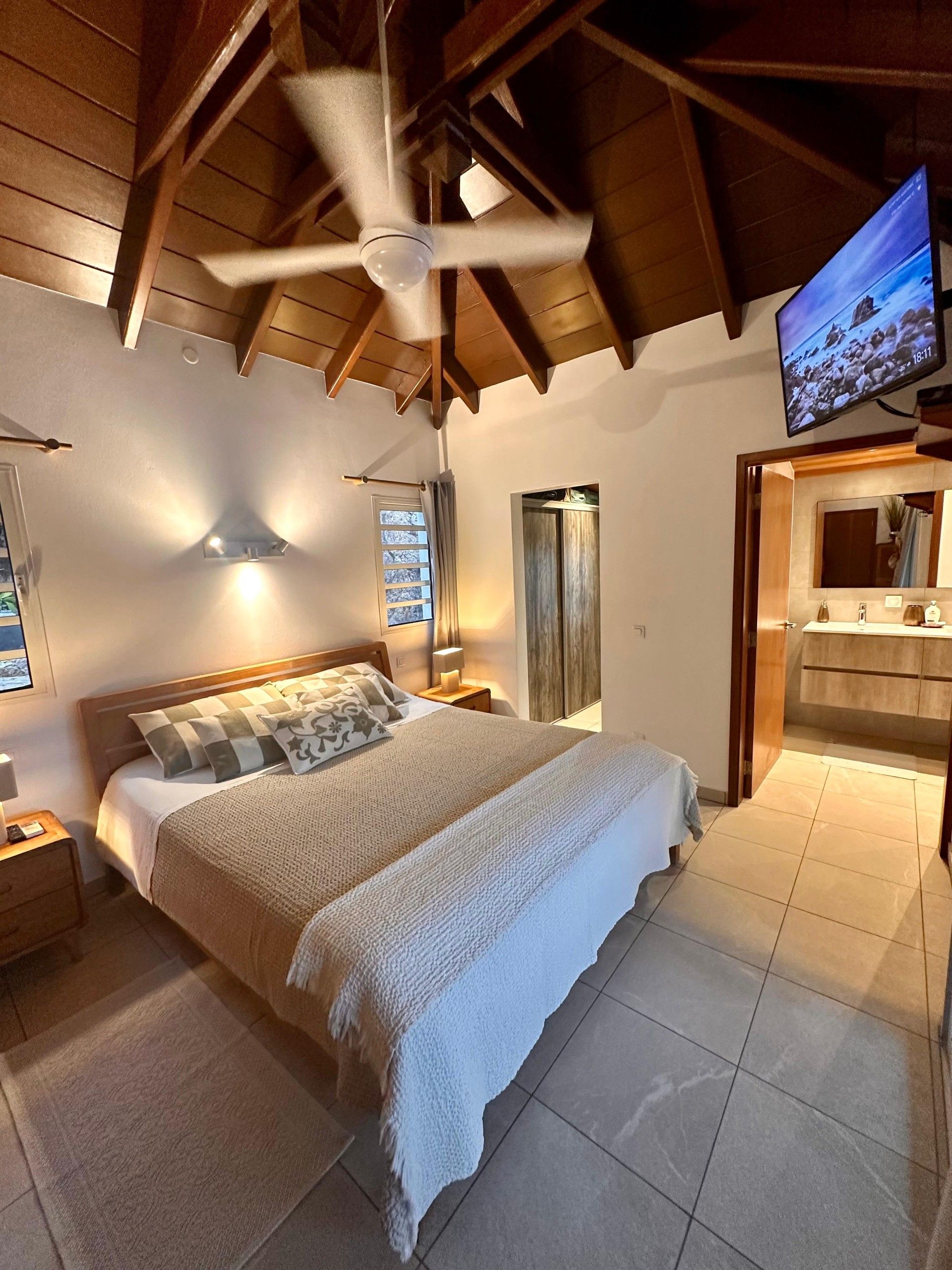 A bedroom with a bed, a ceiling fan, a television, and a bathroom with a mirror and sink.