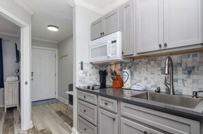 A kitchen with grey cabinets, a stainless steel sink, a microwave, and a tiled backsplash. - Cozy 1 BR in Sea Mist! (Carolina Beach)