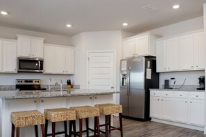 A modern kitchen with white cabinets, stainless steel appliances, a granite countertop, and a built-in island with bar stools. - 🌴Sweet 'N Salty | Walk to Beach | Community Pool🌴 (WindMark Beach)