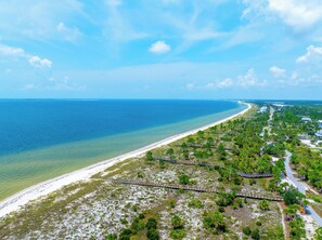A coastal landscape with a beach, clear blue water, and a pathway leading to a building. - 🌴Sweet 'N Salty | Walk to Beach | Community Pool🌴 (WindMark Beach)