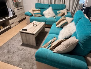 A teal sofa with striped pillows, a wooden coffee table, and a grey rug in a living room. - Apartment in El Rompido with a pool | 3 bedrooms | 3 bathrooms (El Rompido)