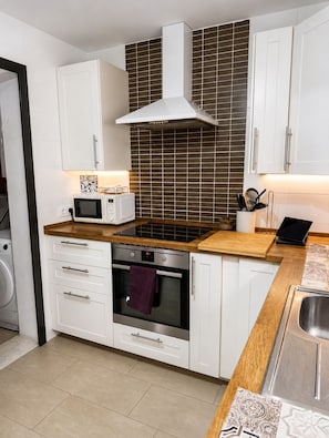 A modern kitchen with white cabinets, a microwave, an oven, and a wooden countertop. - Apartment in El Rompido with a pool | 3 bedrooms | 3 bathrooms (El Rompido)