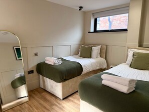 Een slaapkamer met twee bedden, een grote spiegel en een raam met uitzicht op een bakstenen muur.