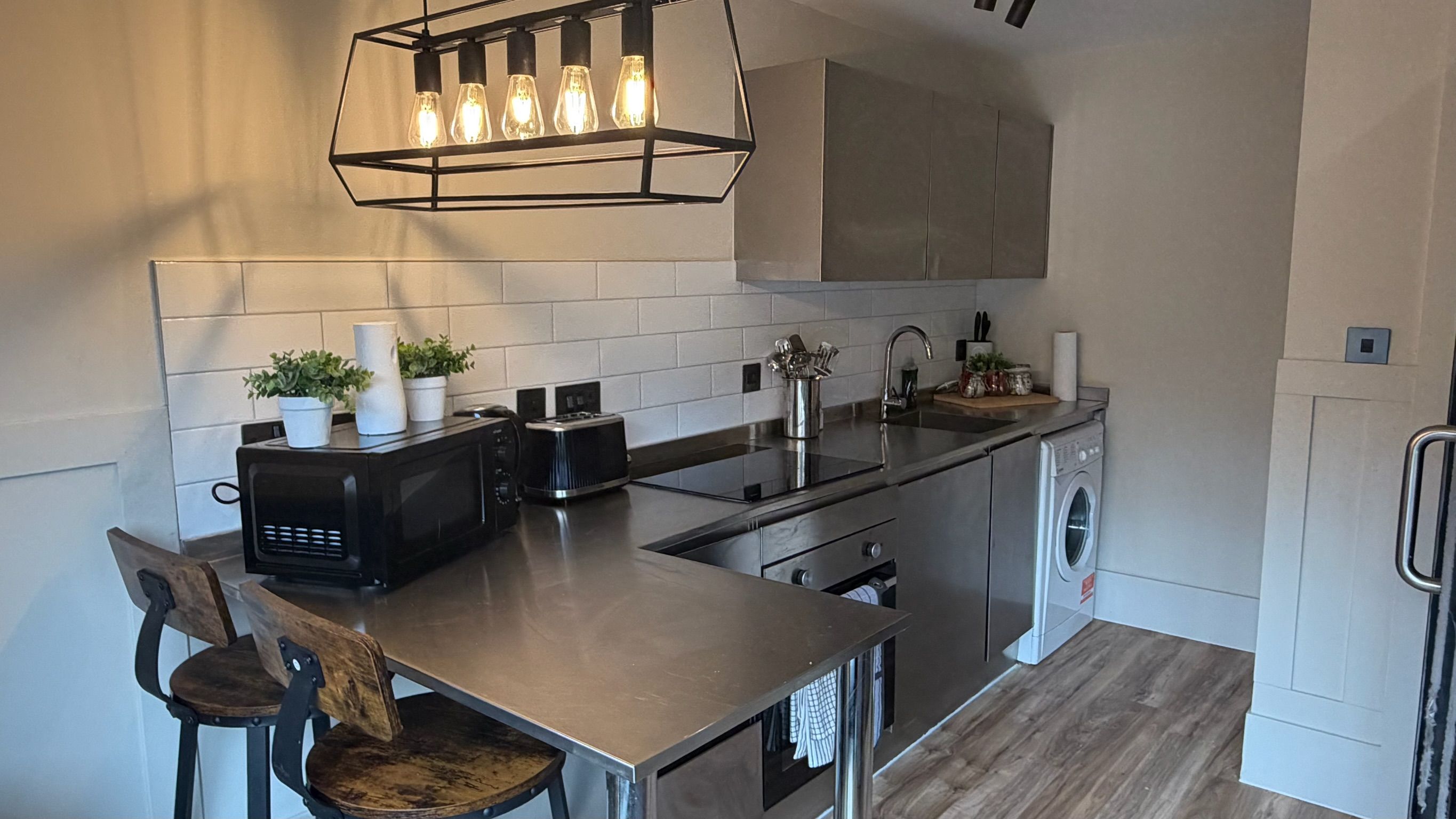 Una cocina moderna con una isla de acero inoxidable, horno empotrado, microondas, tostadora y lavabo.
