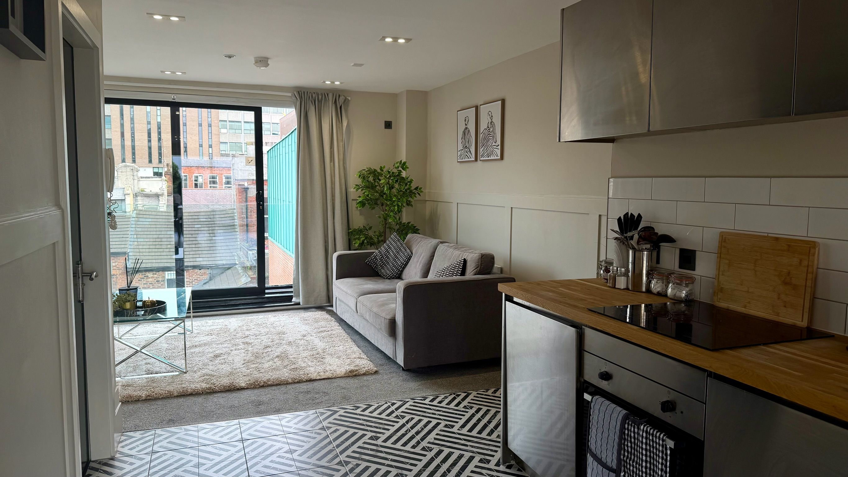 A modern apartment with a living area, kitchenette, and a sliding glass door leading to a balcony.