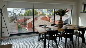Een eethoek met een tafel voor vier personen, een groot raam met uitzicht op gebouwen en een vloer met een patroon.