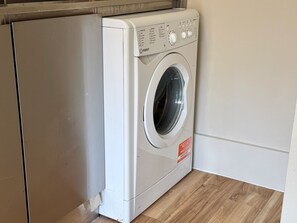 Een voorlader wasmachine in een hoek van een kamer met houten vloer.