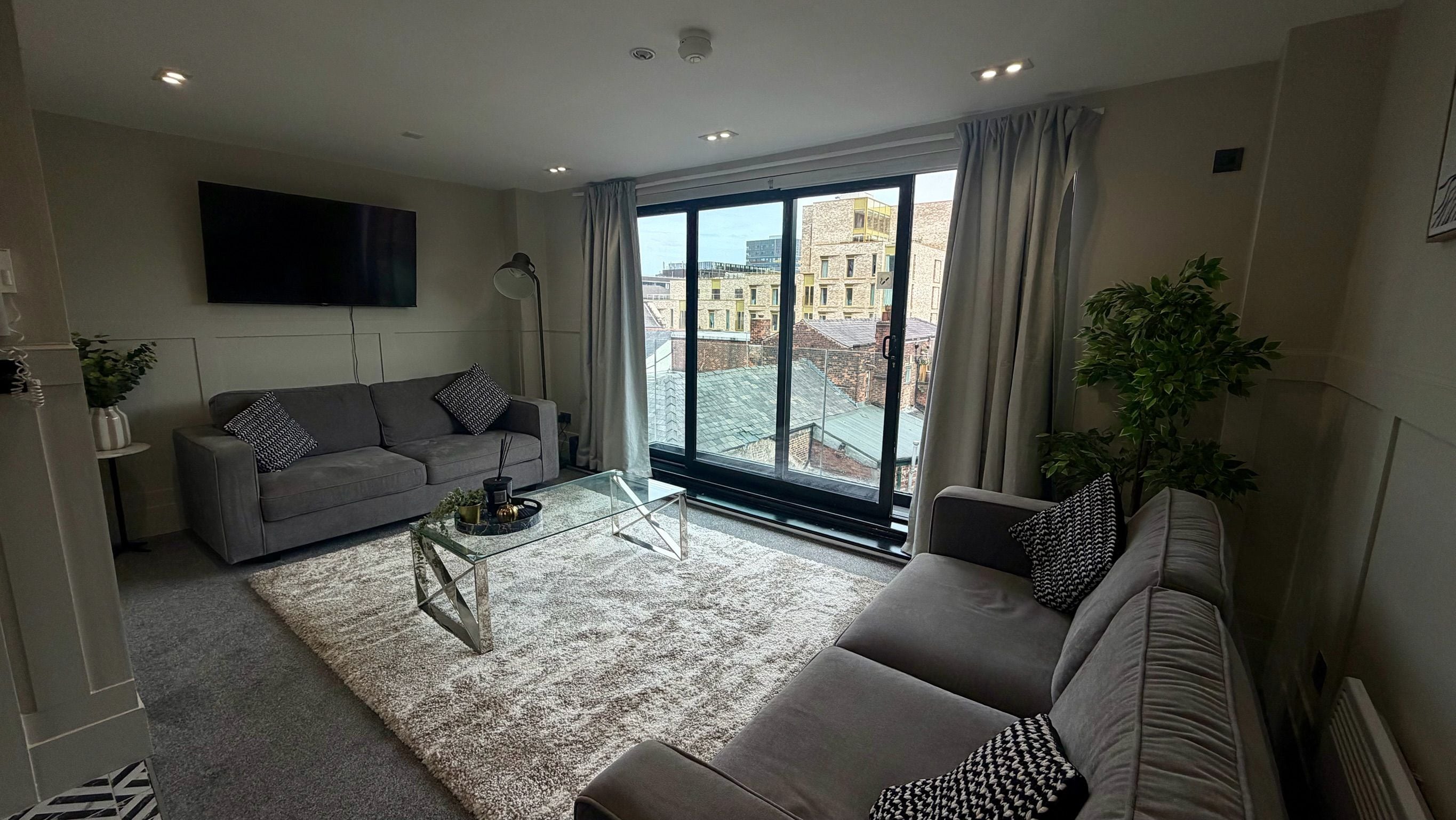 Una sala de estar moderna con un sofá gris, una mesa de centro de vidrio y un ventanal con vistas a la ciudad.