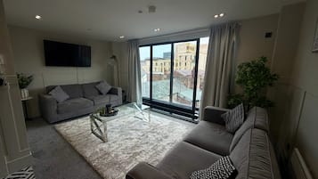 Una sala de estar moderna con un sofá gris, una mesa de centro de vidrio y un ventanal con vistas a la ciudad.