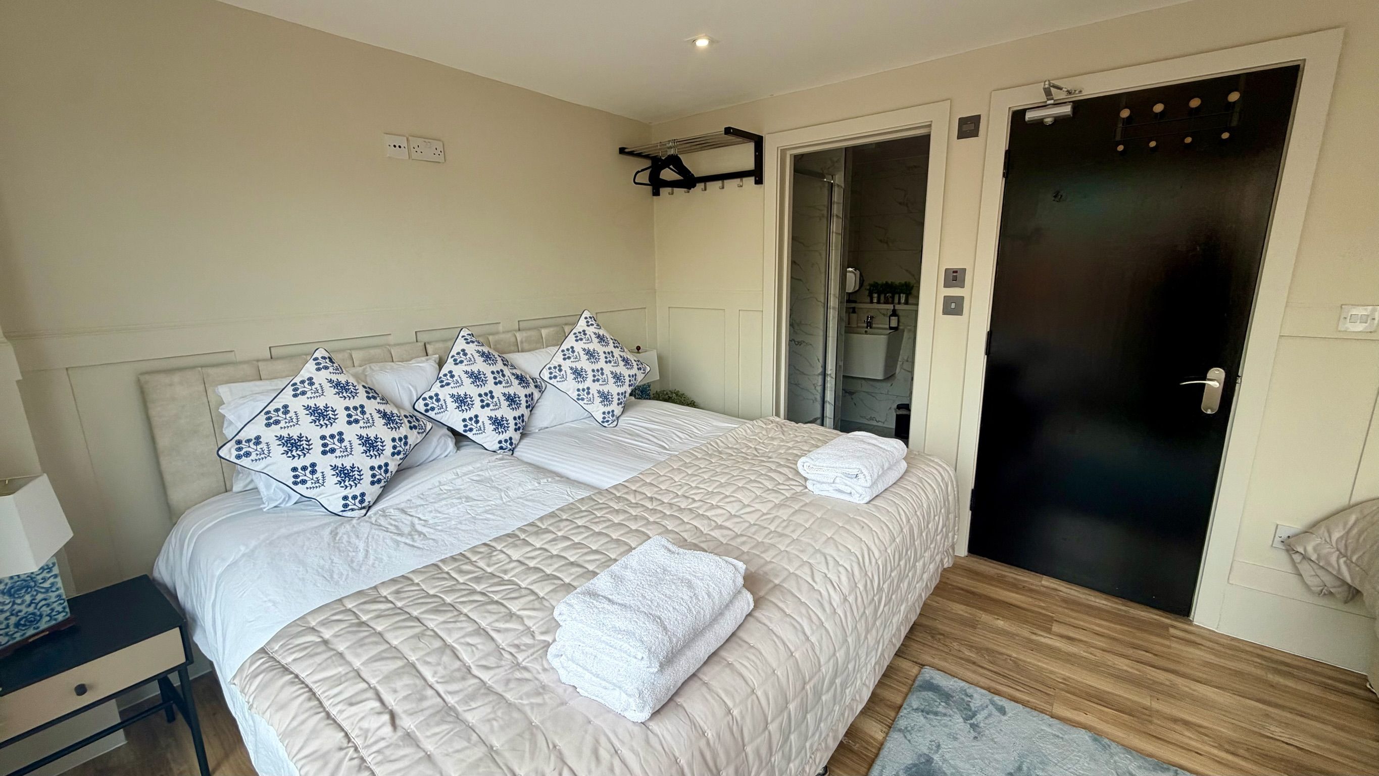 A bedroom with a bed, pillows, a nightstand, a door, and a bathroom visible through an open door.