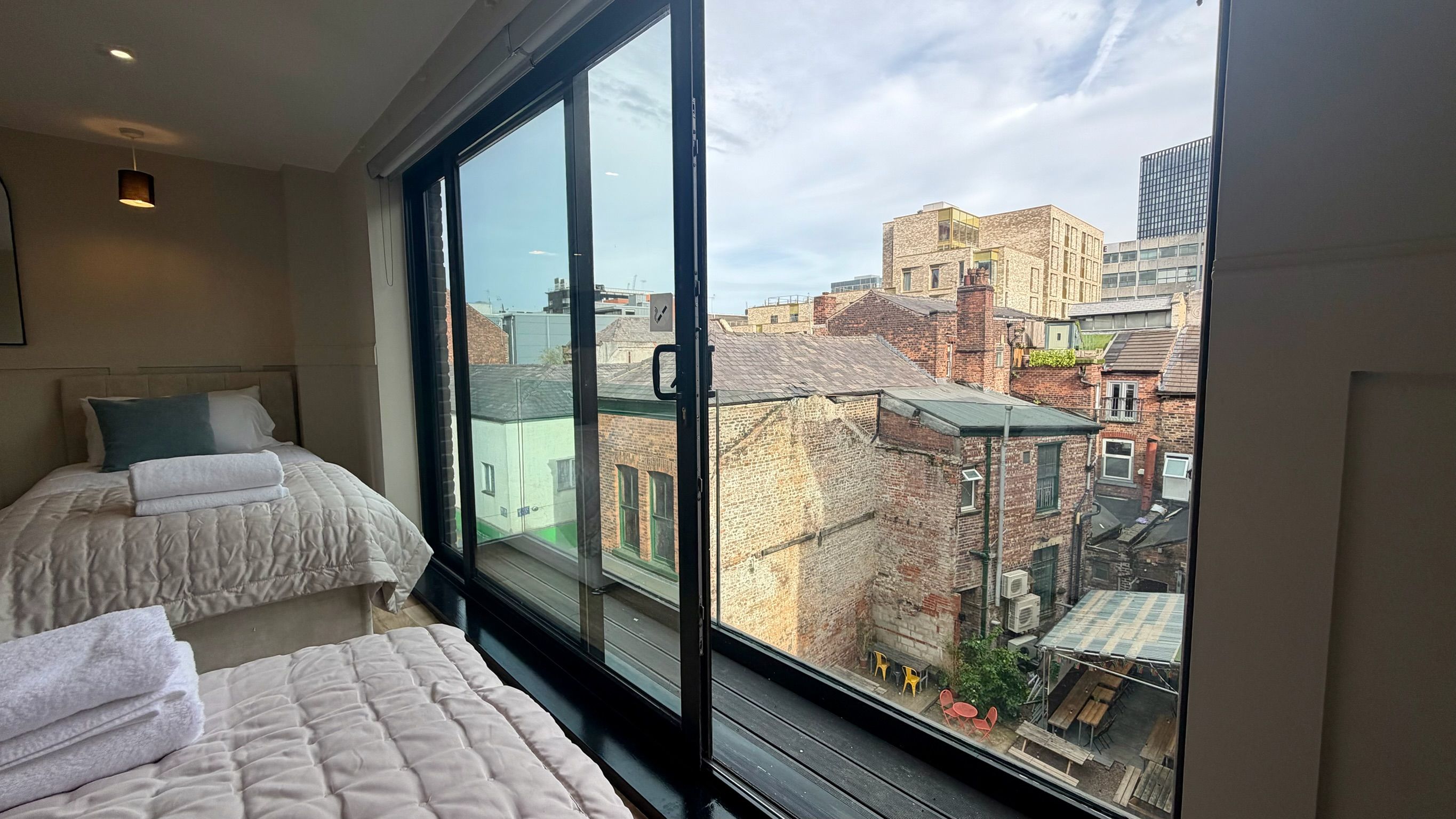 Habitación de hotel con un ventanal grande, dos camas y vistas a la ciudad.