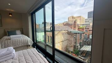 Habitación de hotel con un ventanal grande, dos camas y vistas a la ciudad.