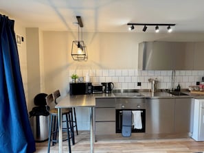 Una cocina moderna con electrodomésticos de acero inoxidable, una zona de comedor con taburetes y una lámpara colgante.