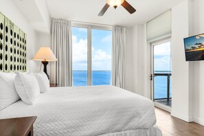 Ein Hotelzimmer mit einem großen Bett, einem Deckenventilator, Blick auf das Meer und einem Gemälde an der Wand.