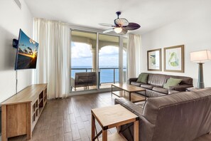 Ein modernes Wohnzimmer mit einer Couch, einem Couchtisch, einem Fernseher und einem Balkon mit Meerblick.