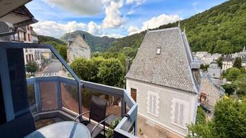 A balcony with a table and chairs, overlooking a village with traditional buildings and a mountainous backdrop.