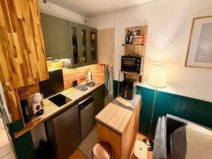 Cozinha compacta com bancada de madeira, pia, lava-louças, cafeteira e micro-ondas.