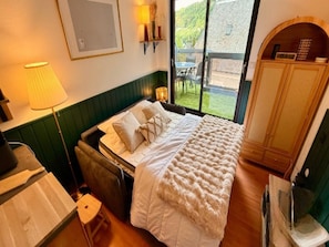 Un dormitorio con cama, una mesita, una silla, una lámpara y vistas al exterior.
