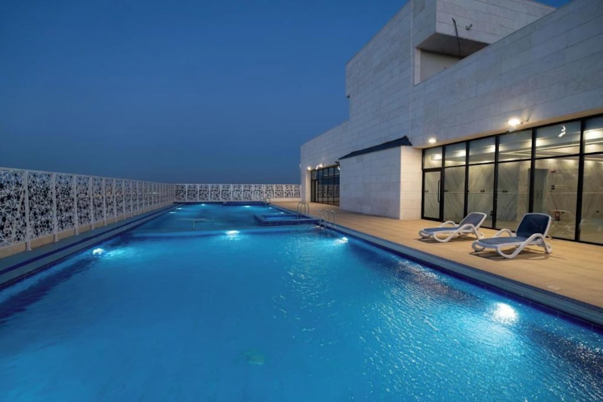 Una piscina interior con vistas despejadas al cielo, un área de descanso junto a la piscina y una fachada de edificio moderna.