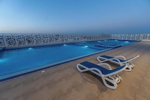 Una piscina con solárium empedrado, dos sillones de descanso y una valla decorativa.