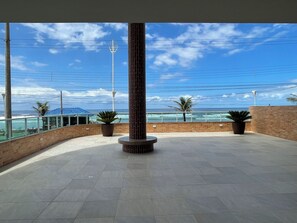An outdoor terrace with a view of the ocean, featuring a brick wall, potted plants, and a tall column. - 2 bedroom apartment, 1 suite, perfect location, new building, beachfront, downtown. (Mongaguá)